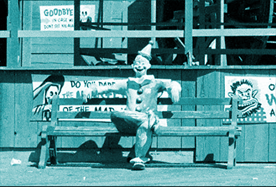 A dilapidated statue of a clown sits on a park bench